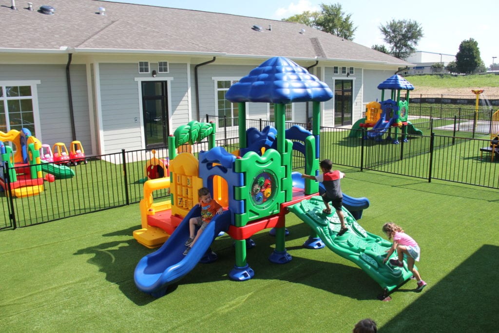 UltraPlay Discovery Center Playground from a high angle perspective on synthetic lawn turf safety surfacing, surrounded by aluminum black fencing